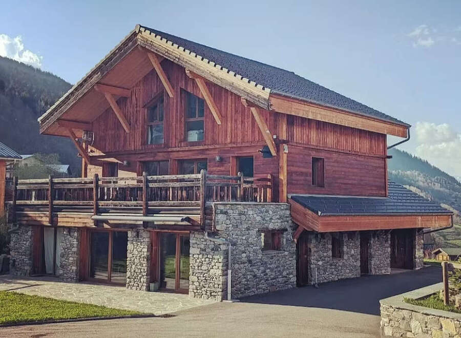 Experience luxury mountain living in this stunning wooden chalet, featuring a spacious balcony with breathtaking views and a rustic stone foundation.