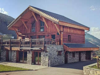 Experience luxury mountain living in this stunning wooden chalet, featuring a spacious balcony with breathtaking views and a rustic stone foundation.