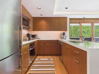 This modern kitchen features sleek, warm wood cabinetry complemented by a clean white countertop and stainless steel appliances.