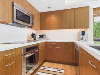 Experience modern luxury in this sleek kitchen, featuring warm wood cabinetry and a pristine white countertop.