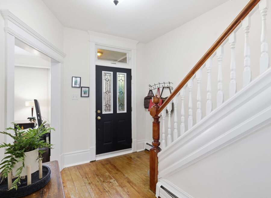 Step into this charming entryway featuring a classic black door with stained glass accents, leading to a beautifully maintained staircase with a rich wooden handrail.
