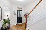 Step into this charming entryway featuring a classic black door with stained glass accents, leading to a beautifully maintained staircase with a rich wooden handrail.