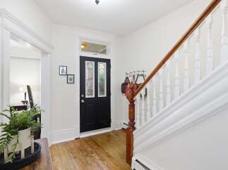 Step into this charming entryway featuring a classic black door with stained glass accents, leading to a beautifully maintained staircase with a rich wooden handrail.