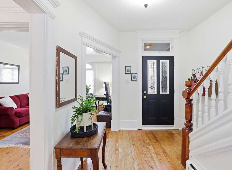 Step into this charming entryway featuring a classic black front door with decorative glass panels, leading to a bright and airy staircase.