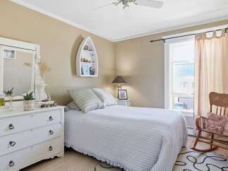 This charming bedroom features a cozy bed with striped bedding and a ruffled skirt, complemented by a white dresser adorned with decorative items.