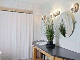 This bathroom features a white tiled shower with a white shower curtain, a dark countertop vanity with a white sink, and two oval mirrors above.