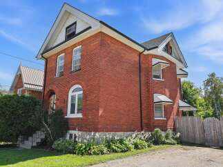Charming red brick home featuring a classic architectural style with a prominent arched window and awnings over the upper-level windows.