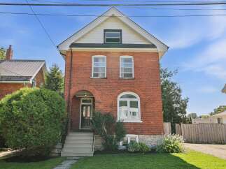 Charming red brick home featuring a classic arched entryway and a large bay window on the main floor.