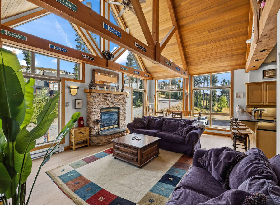 Experience breathtaking mountain views from this stunning living room, featuring a grand stone fireplace and vaulted wooden ceilings.