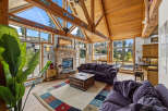 Experience breathtaking mountain views from this stunning living room, featuring a grand stone fireplace and vaulted wooden ceilings.