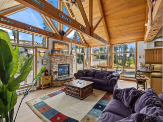 Experience breathtaking mountain views from this stunning living room, featuring a grand stone fireplace and vaulted wooden ceilings.