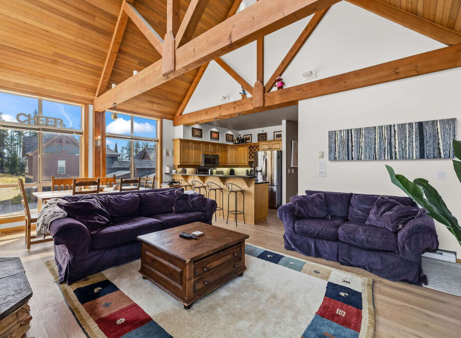 Experience the ultimate mountain retreat with this stunning living space, featuring a soaring vaulted ceiling with exposed wooden beams and a wall of windows offering breathtaking views.