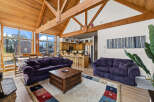 Experience the ultimate mountain retreat with this stunning living space, featuring a soaring vaulted ceiling with exposed wooden beams and a wall of windows offering breathtaking views.