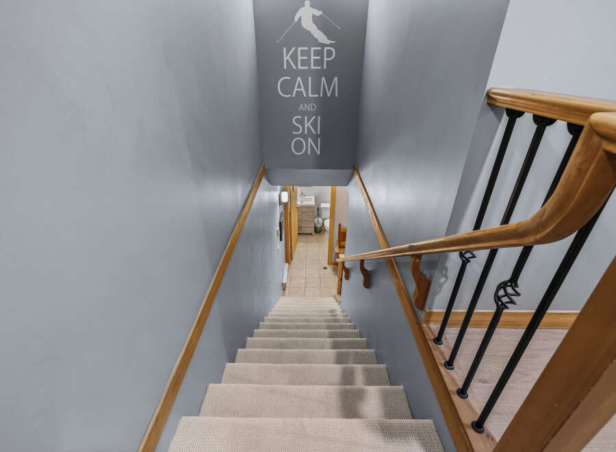 Descend into comfort and style with this carpeted staircase, featuring a smooth wooden handrail and elegant black balusters.