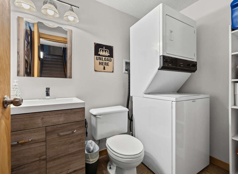 This compact bathroom and laundry area features a modern vanity with ample storage, a convenient toilet, and a stacked washer and dryer.