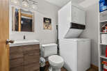 This compact bathroom and laundry area features a modern vanity with ample storage, a convenient toilet, and a stacked washer and dryer.