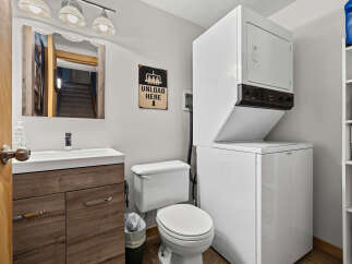 This compact bathroom and laundry area features a modern vanity with ample storage, a convenient toilet, and a stacked washer and dryer.