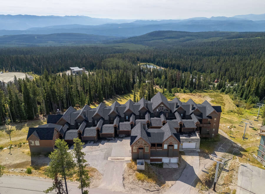 Discover this stunning mountain property featuring a complex of modern chalets with dark roofs and rich wood exteriors, nestled amidst a dense pine forest.