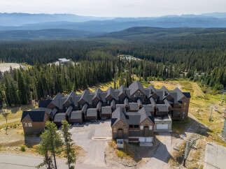 Discover this stunning mountain property featuring a complex of modern chalets with dark roofs and rich wood exteriors, nestled amidst a dense pine forest.