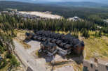 Discover this stunning mountain property featuring multiple townhome-style residences with dark pitched roofs and warm wood exteriors, nestled amidst a dense evergreen forest.