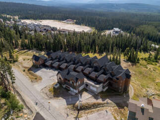 Discover this stunning mountain property featuring multiple townhome-style residences with dark pitched roofs and warm wood exteriors, nestled amidst a dense evergreen forest.