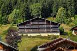 Experience the charm of alpine living in this stunning multi-story chalet nestled amidst lush green hills and a dense forest backdrop.