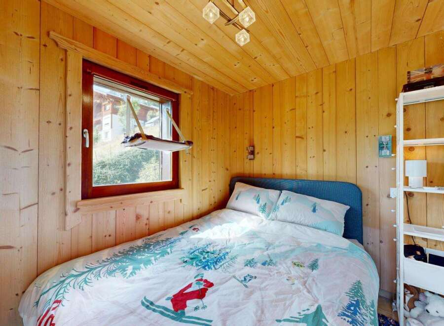 Cozy wooden cabin bedroom featuring a comfortable bed with charming ski-themed bedding and a picturesque window view.