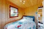 Cozy wooden cabin bedroom featuring a comfortable bed with charming ski-themed bedding and a picturesque window view.