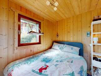 Cozy wooden cabin bedroom featuring a comfortable bed with charming ski-themed bedding and a picturesque window view.