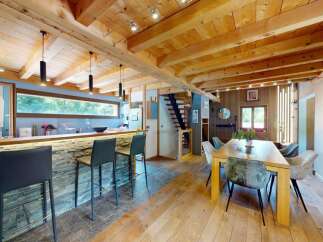 Experience rustic charm and modern comfort in this stunning open-plan living space, featuring a sleek kitchen island with stone accents and comfortable bar stools.