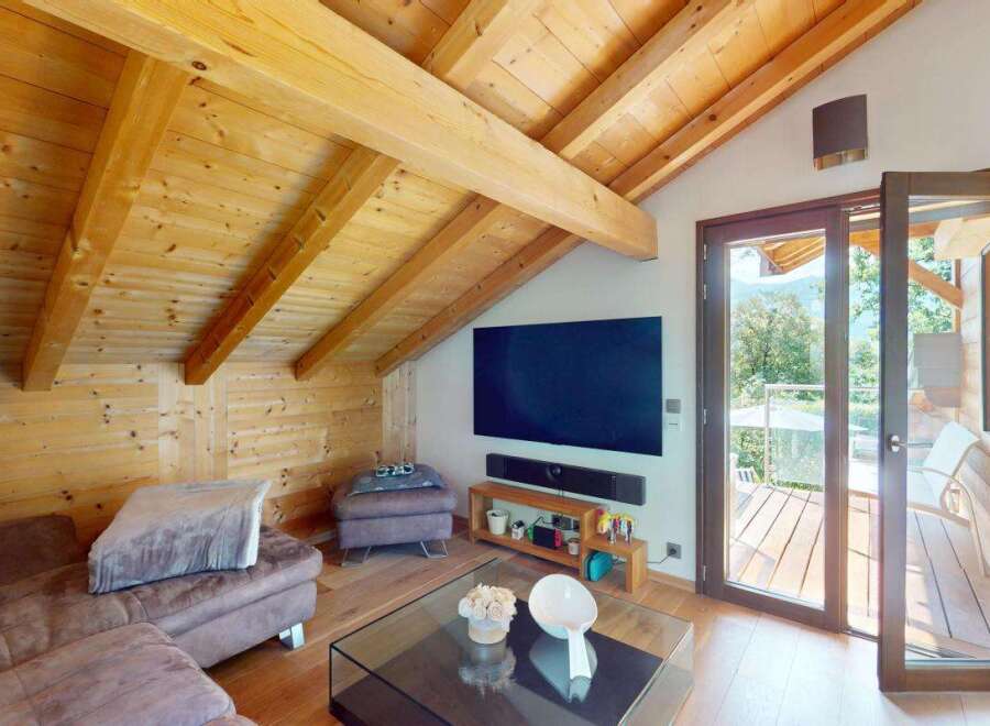 Experience rustic charm and modern comfort in this stunning attic living space, featuring exposed wooden beams and a cozy sectional sofa.
