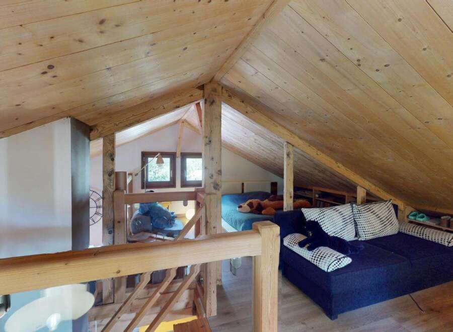 Discover this charming attic space, featuring a cozy sleeping area with a plush bed and a comfortable seating area with a dark blue sofa adorned with patterned pillows.