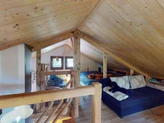 Discover this charming attic space, featuring a cozy sleeping area with a plush bed and a comfortable seating area with a dark blue sofa adorned with patterned pillows.