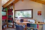 Discover a cozy home office space featuring a large window with scenic views, a built-in bookshelf filled with binders and books, and a functional desk area with a laptop and printer.
