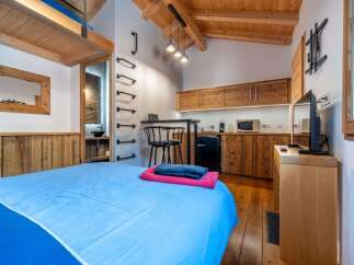 Experience cozy living in this charming studio apartment, featuring a comfortable bed with vibrant blue linens and a convenient kitchenette.