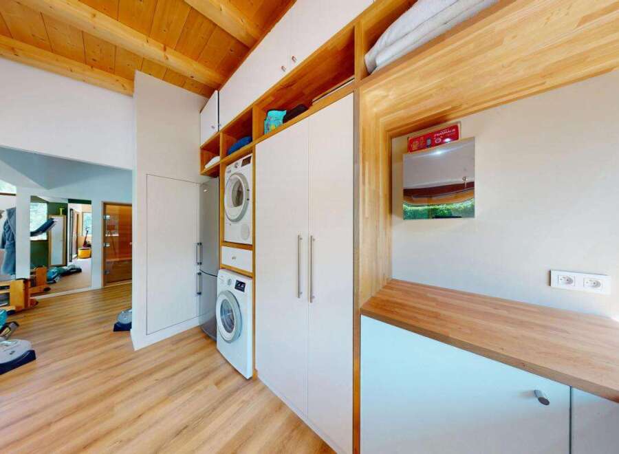 Discover a modern laundry room featuring stacked washer and dryer units, ample storage with white cabinets, and a sleek wooden countertop.