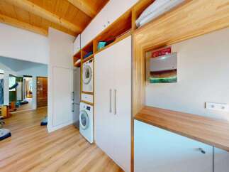 Discover a modern laundry room featuring stacked washer and dryer units, ample storage with white cabinets, and a sleek wooden countertop.