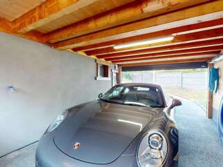 This spacious garage offers ample parking for your vehicles, featuring a sleek grey Porsche.