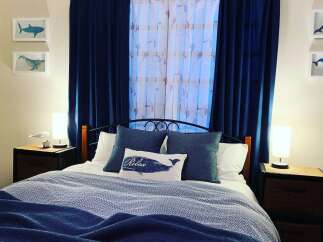 Discover this charming bedroom featuring a comfortable queen-size bed adorned with plush navy blue pillows and a decorative throw pillow with a whale motif.