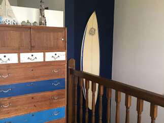 This coastal-themed staircase features a charming wooden dresser with blue and white drawers, complemented by nautical decor like a sailboat and lighthouse.