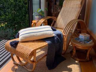 Experience serene relaxation in this sun-drenched reading nook, featuring a comfortable rattan rocking chair and ottoman.