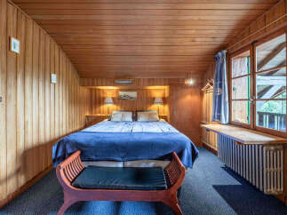 Experience cozy living in this charming wood-paneled bedroom, featuring a comfortable queen-sized bed adorned with a plush blue blanket.