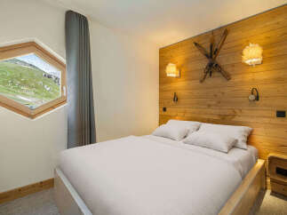 Experience cozy mountain living in this charming bedroom featuring a unique hexagonal window with stunning alpine views.