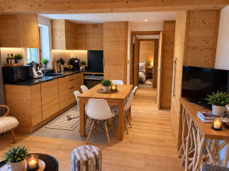 Experience modern alpine living in this beautifully appointed apartment, featuring a sleek, wood-paneled kitchen with integrated appliances and a cozy dining area perfect for family meals.