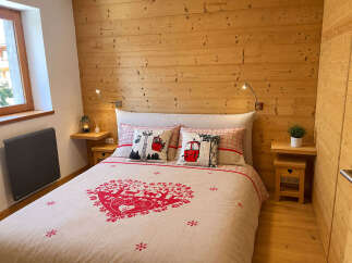Experience cozy mountain living in this charming bedroom featuring warm, wood-paneled walls and a comfortable bed adorned with festive ski-themed pillows and a heart-shaped duvet cover.