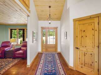 Step into this inviting entryway featuring a warm wooden ceiling and a striking runner rug that guides you towards a beautiful glass-paneled front door.