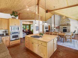 Experience rustic charm in this spacious open-concept living area, featuring a stunning stone fireplace and vaulted wood-paneled ceilings.