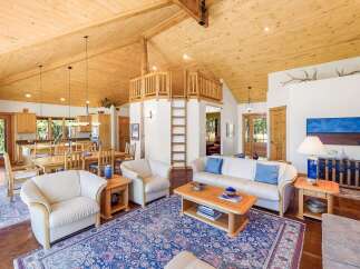 Experience rustic charm in this spacious living area featuring a vaulted wood-paneled ceiling and a unique loft accessible by ladder.
