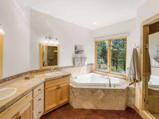 Indulge in relaxation in this luxurious bathroom featuring a spacious corner jetted tub with a stunning view of the surrounding trees.