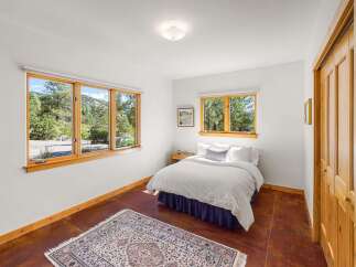 Experience serene living in this charming bedroom, featuring large wooden-framed windows that offer breathtaking views of the surrounding natural landscape.